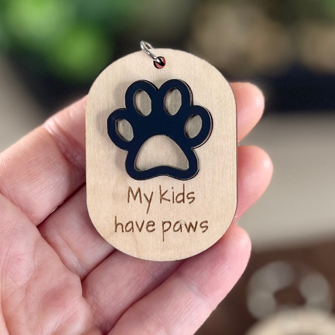 Hand holding My Kids Have Paws maple keychain showing black acrylic paw print detail"