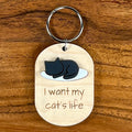I Want My Cat's Life laser-engraved maple wood keychain with black acrylic sleeping cat silhouette on wood background