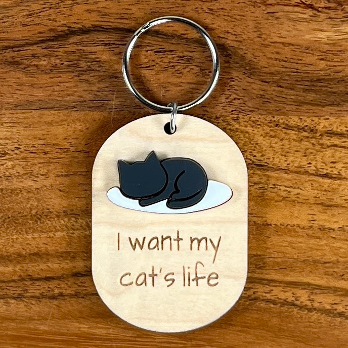 I Want My Cat's Life laser-engraved maple wood keychain with black acrylic sleeping cat silhouette on wood background