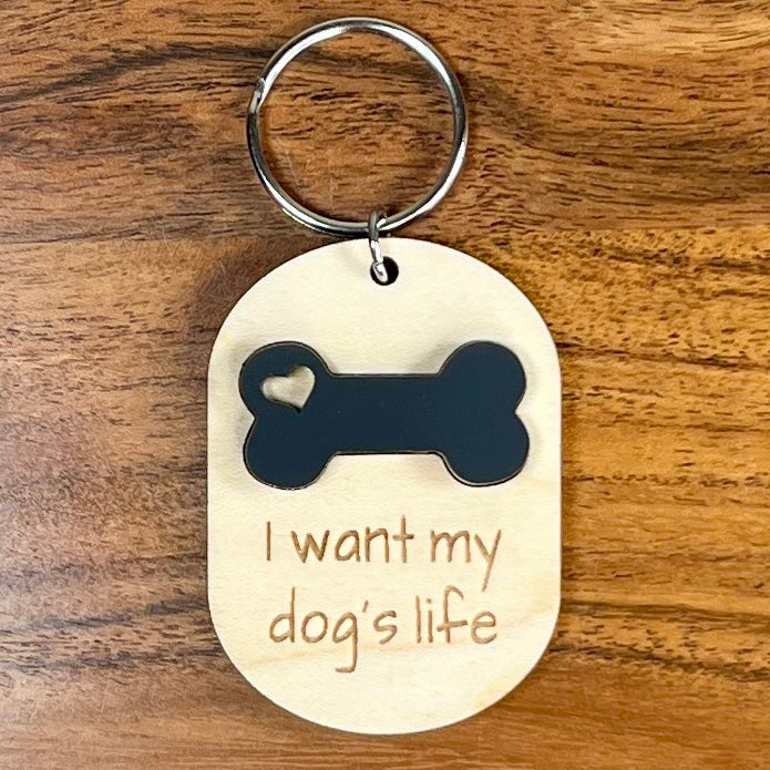 I Want My Dog's Life laser-engraved maple wood keychain with black acrylic dog bone on wood background