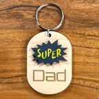 Super Dad laser-cut maple wood keychain with black and yellow acrylic comic burst and engraved text.