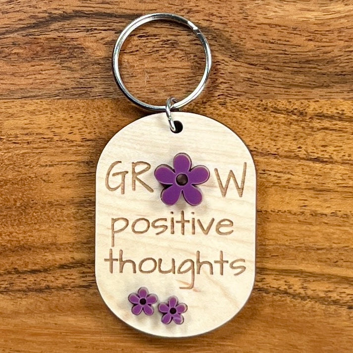 Grow Positive Thoughts laser-engraved maple wood keychain with purple acrylic daisy flower accents on wood background