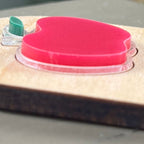 Side view of an oval wooden keychain with a layered red and green acrylic apple, highlighting the 3D effect of the design.