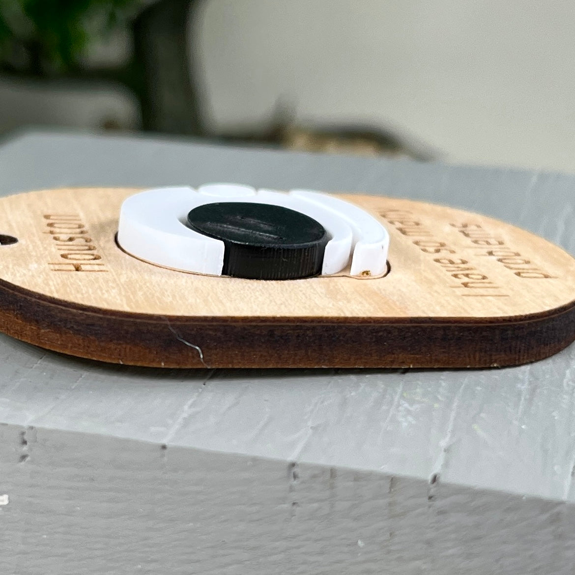 Side view of a wooden keychain with a layered white and black acrylic space helmet, highlighting the 3D effect.