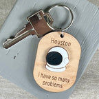 Wooden keychain with acrylic space helmet engraved 'Houston, I have so many problems,' with a metal key on a gray surface.