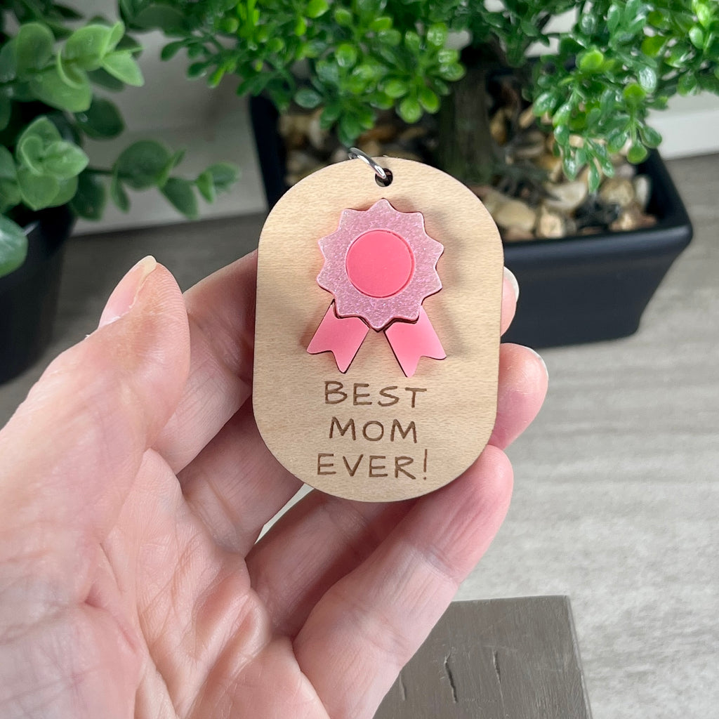 Hand holding Best Mom Ever wooden keychain with pink acrylic daisy detail.