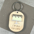 Oval wooden keychain with lemon acrylic drip cake, engraved 'I brake for cake,' on a  brown surface with a metal split ring.