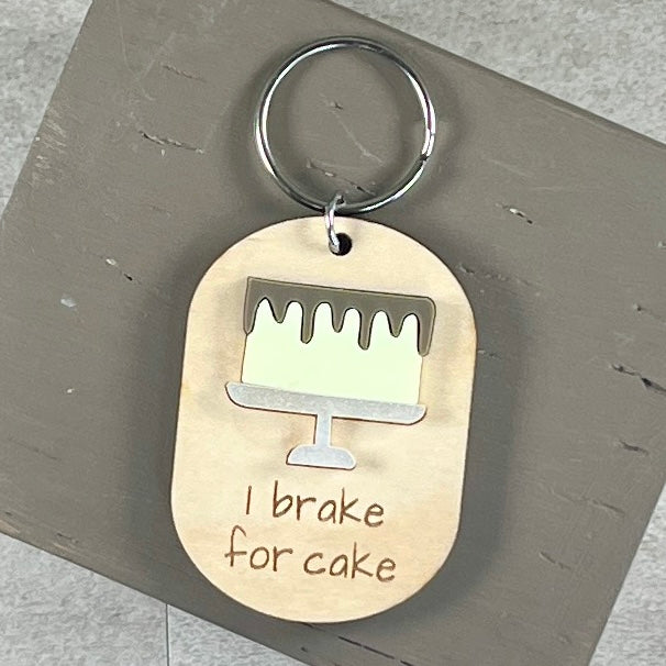 Oval wooden keychain with lemon acrylic drip cake, engraved 'I brake for cake,' on a  brown surface with a metal split ring.