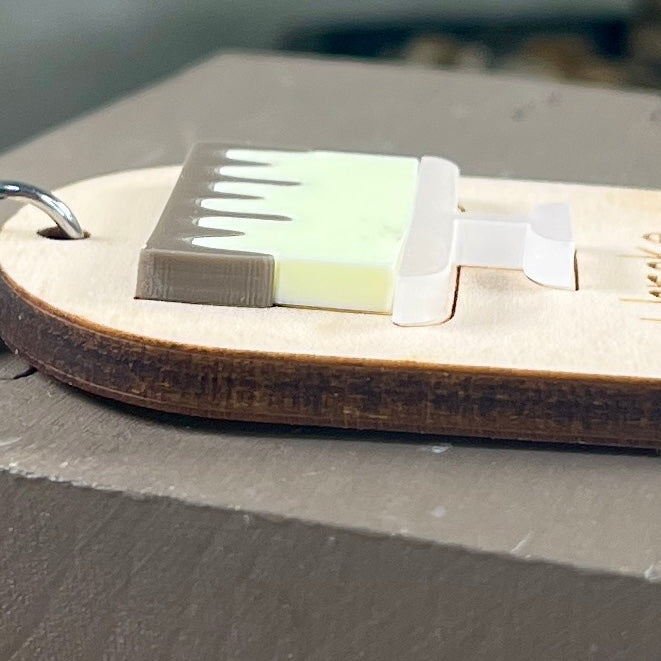 Side view of an oval wooden keychain with a layered lemon acrylic drip cake, highlighting the 3D effect of the design. 