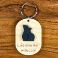 Life Is Better With Cats laser-engraved maple wood keychain with black acrylic cat duo silhouette on wood background