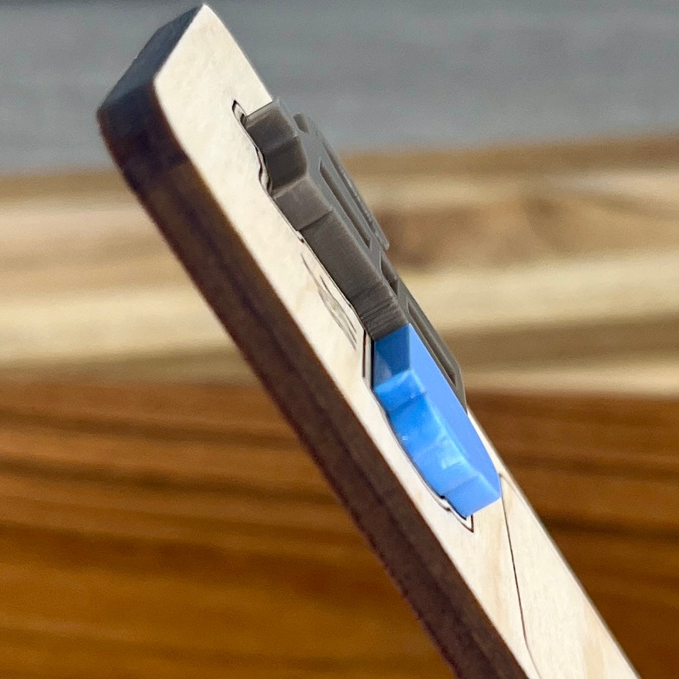 A side view close-up of a wooden bookmark highlighting the 3D effect of the layered acrylic coffee mug and moka pot, photographed against a blurred wood and gray background.