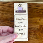 Hand holding Sip Coffee Read Books Stay Cozy birch bookmark showing ash rose and mauve acrylic detail