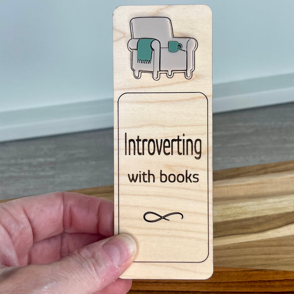 Hand holding Introverting with Books birch bookmark showing sage acrylic chair and mug detail