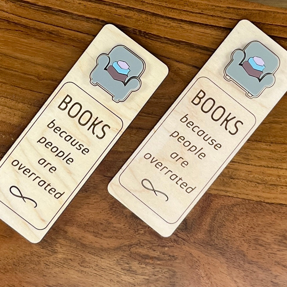 Two rectangular wooden bookmarks with the phrase 'BOOKS because people are overrated' engraved on a warm wood tabletop.