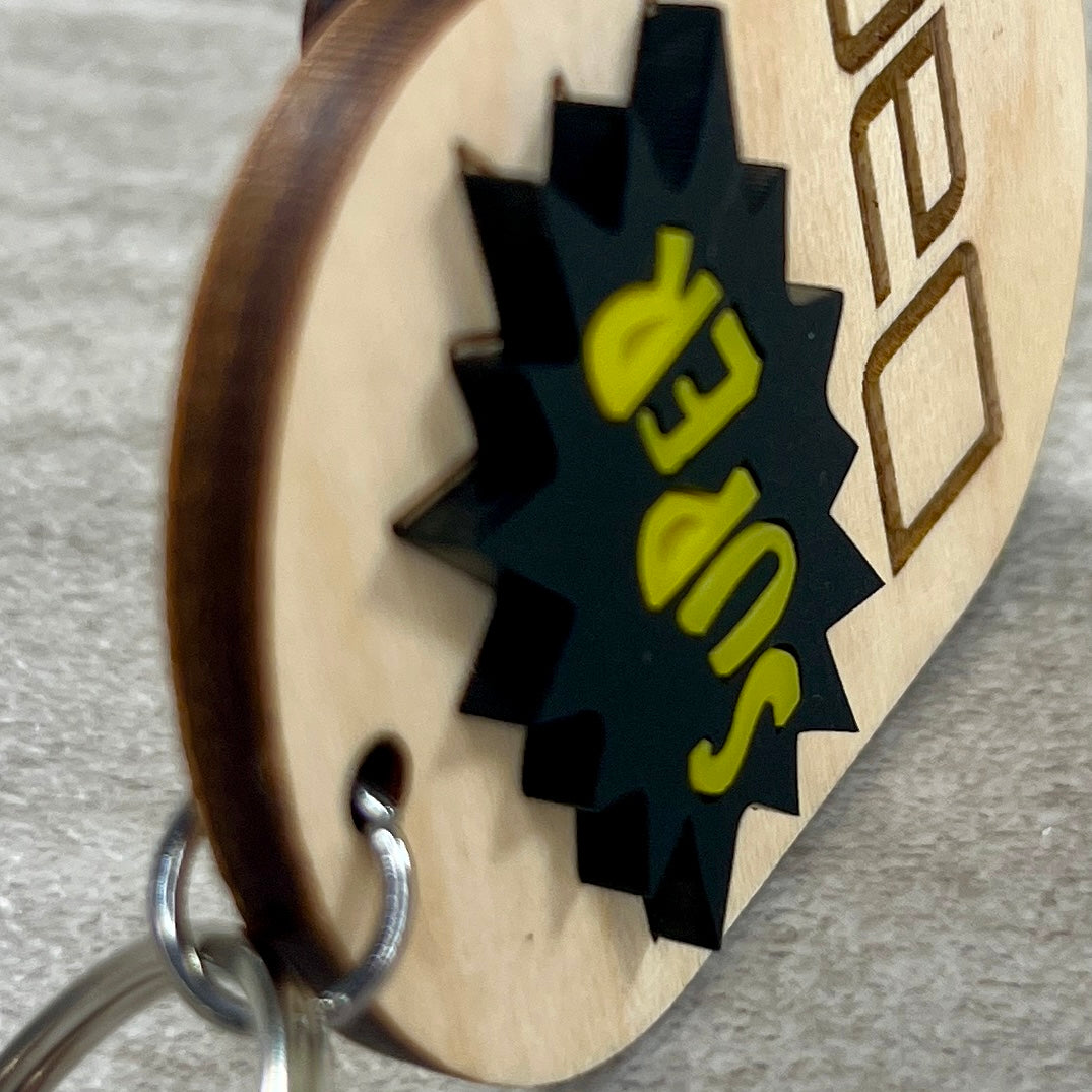 Side view of Super Dad maple wood keychain with black and yellow acrylic comic burst.