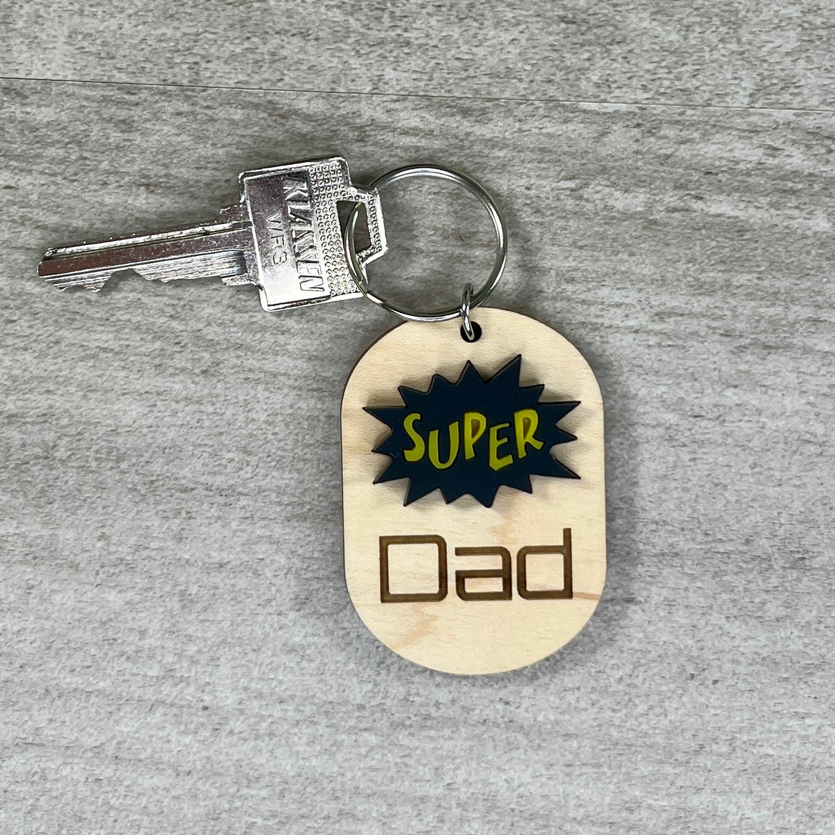 Super Dad engraved wood keychain with silver key ring on neutral background.