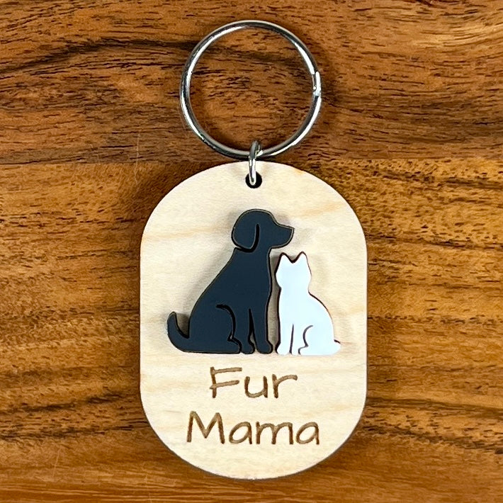Oval wooden keychain with black and white acrylic dog and cat, engraved 'Fur Mama,' on a wood surface with a metal split ring.