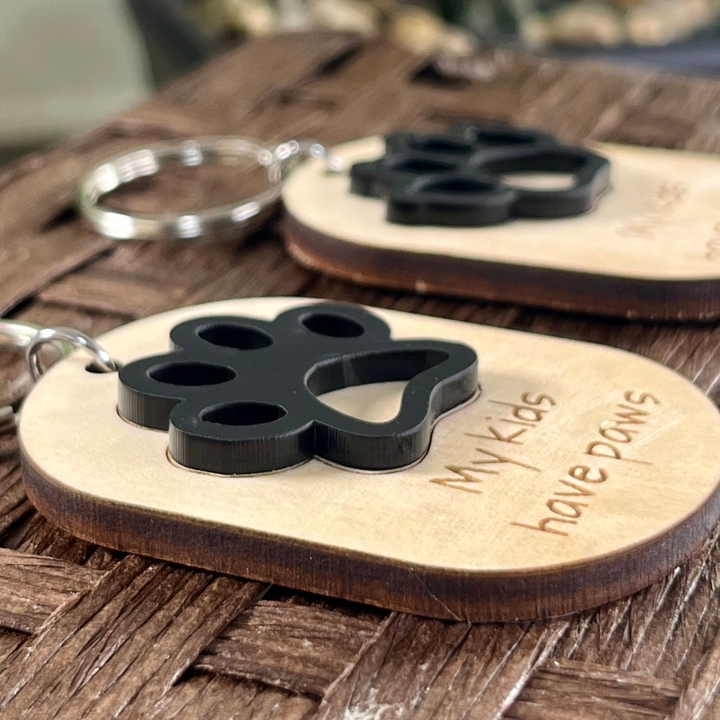 Side view of My Kids Have Paws maple keychain showing dimensional layered black acrylic paw print detail