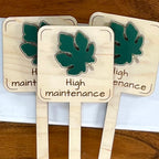 Three High Maintenance maple wood plant stakes with forest green acrylic fig leaf fanned out