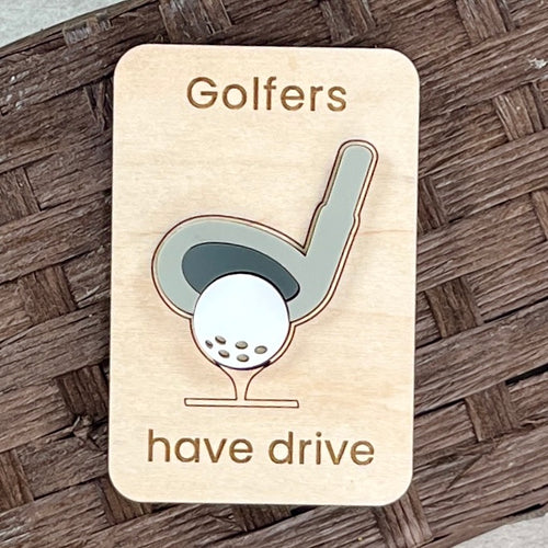 A rectangular wooden golf-themed magnet with rounded corners, laser-engraved with the words 'Golfers have drive' and a stylized acrylic golf club and ball design. The sign is placed on a brown woven wicker surface.