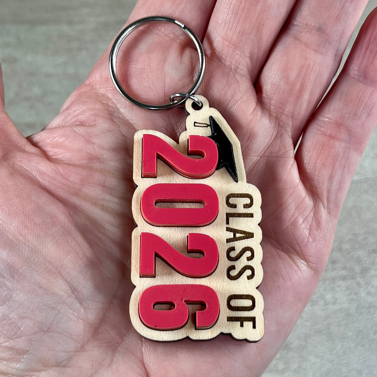 Hand holding Class of 2026 maple graduation keychain showing acrylic grad cap and watermelon and blue numeral detail
