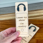 Hand holding Leave Me Alone I'm Reading birch bookmark showing laser-engraved text detail