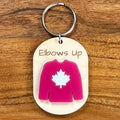 Elbows Up laser-engraved maple wood keychain with red acrylic Canadian hockey jersey on wood background