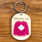 Elbows Up laser-engraved maple wood keychain with red acrylic maple leaf hockey jersey on wood background