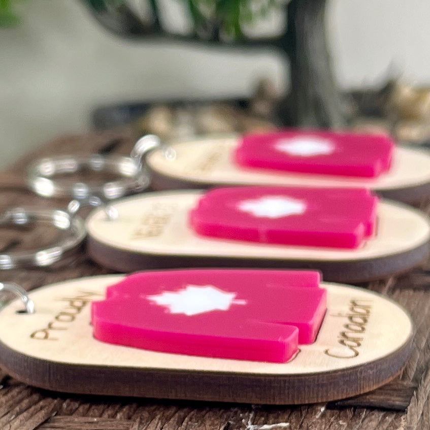 Proudly Canadian maple keychains displayed on wood surface showing engraved text and red acrylic hockey jersey