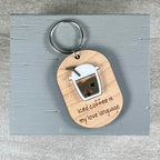 A wooden keychain with a metal split ring, featuring an acrylic coffee cup design and the engraved phrase 'Iced coffee is my love language' on a light wood tag, displayed on a gray painted wooden block.