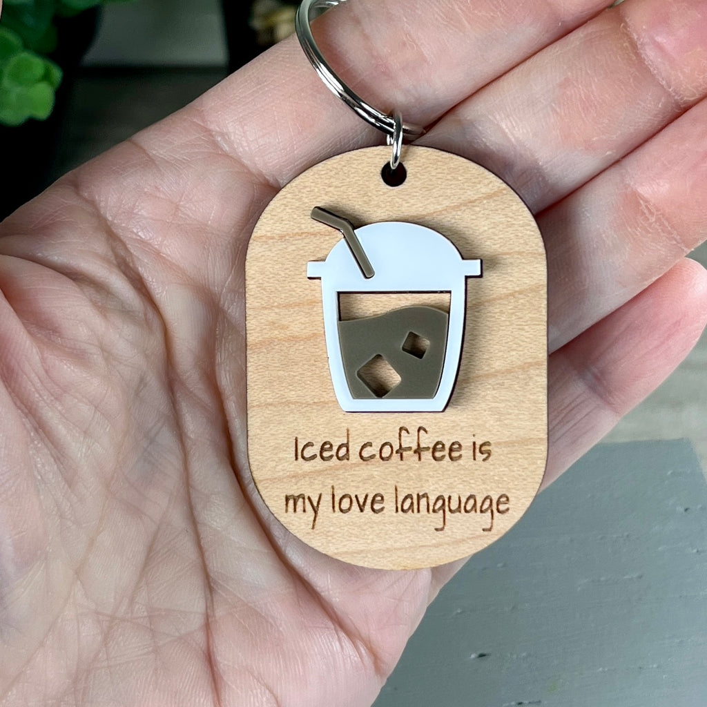 A wooden keychain held in a hand, featuring a layered acrylic coffee cup design and the laser-engraved phrase 'Iced coffee is my love language'.