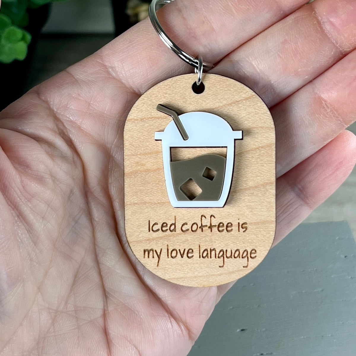 A wooden keychain held in a hand, featuring a layered acrylic coffee cup design and the laser-engraved phrase 'Iced coffee is my love language'.