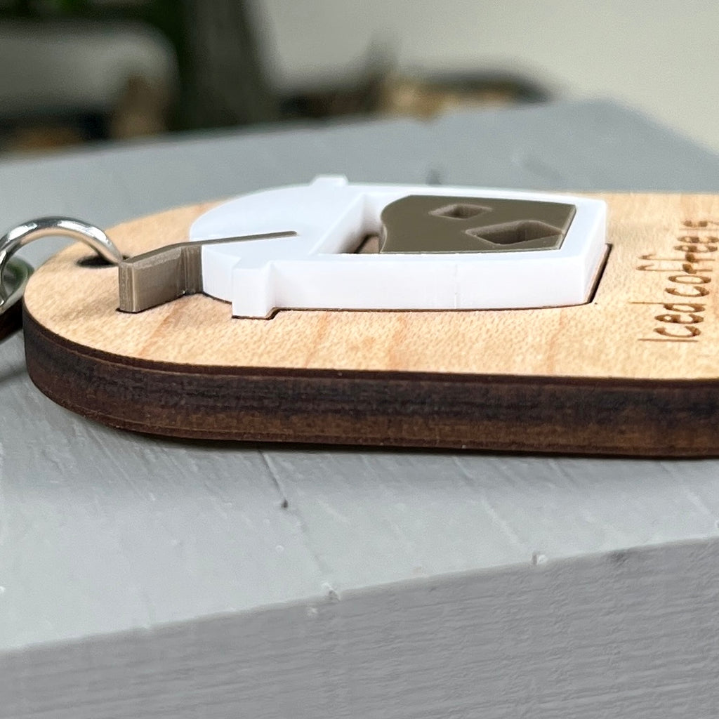 A side view close-up of a wooden engraved keychain with a layered white acrylic iced coffee design, resting on a light gray surface,  showcasing the 3D nature of the product.