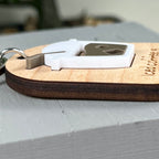 A side view close-up of a wooden engraved keychain with a layered white acrylic iced coffee design, resting on a light gray surface,  showcasing the 3D nature of the product.