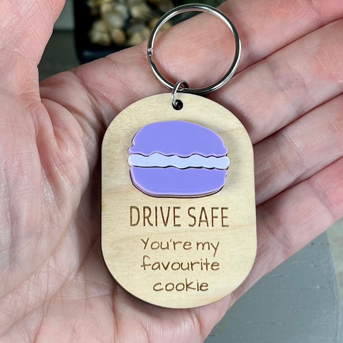 Hand holding Drive Safe maple keychain with purple acrylic macaron on wood background