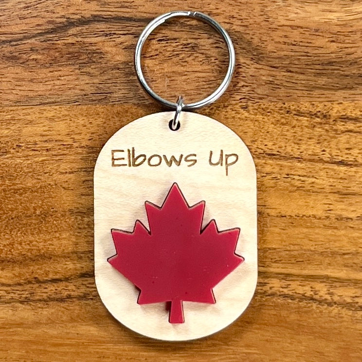 Elbows Up laser-engraved maple wood keychain with red acrylic maple leaf on wood background