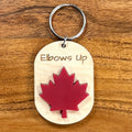 Elbows Up laser-engraved maple wood keychain with red acrylic maple leaf on wood background