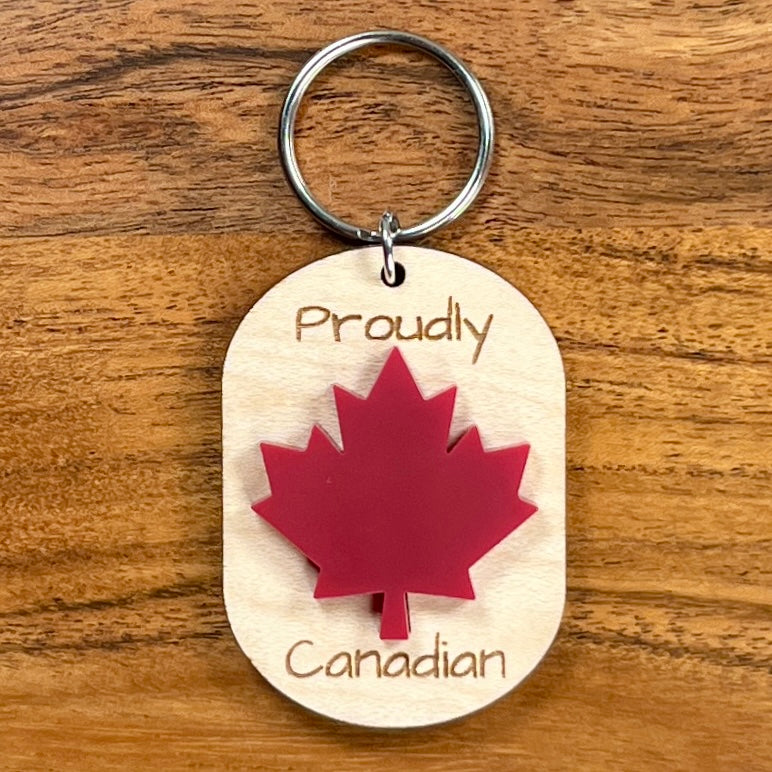 Proudly Canadian laser-engraved maple wood keychain with red acrylic maple leaf on wood background
