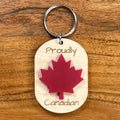 Proudly Canadian laser-engraved maple wood keychain with red acrylic maple leaf on wood background