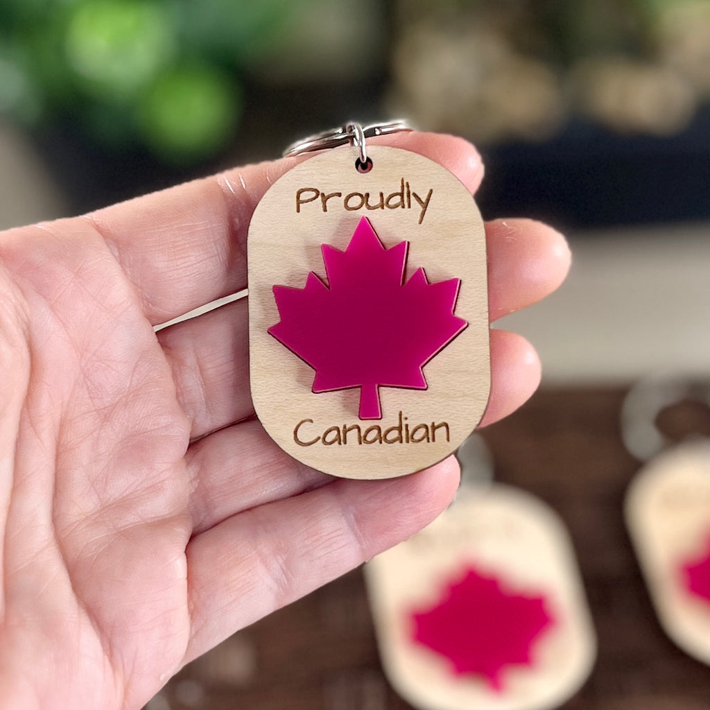 Hand holding Proudly Canadian maple keychain showing red acrylic maple leaf detail
