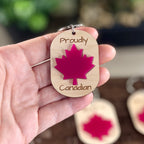 Hand holding Proudly Canadian maple keychain showing red acrylic maple leaf detail