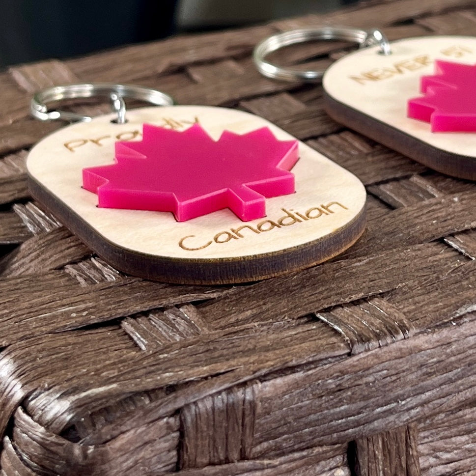 Proudly Canadian maple keychains displayed on wood surface showing engraved text and red acrylic maple leaf