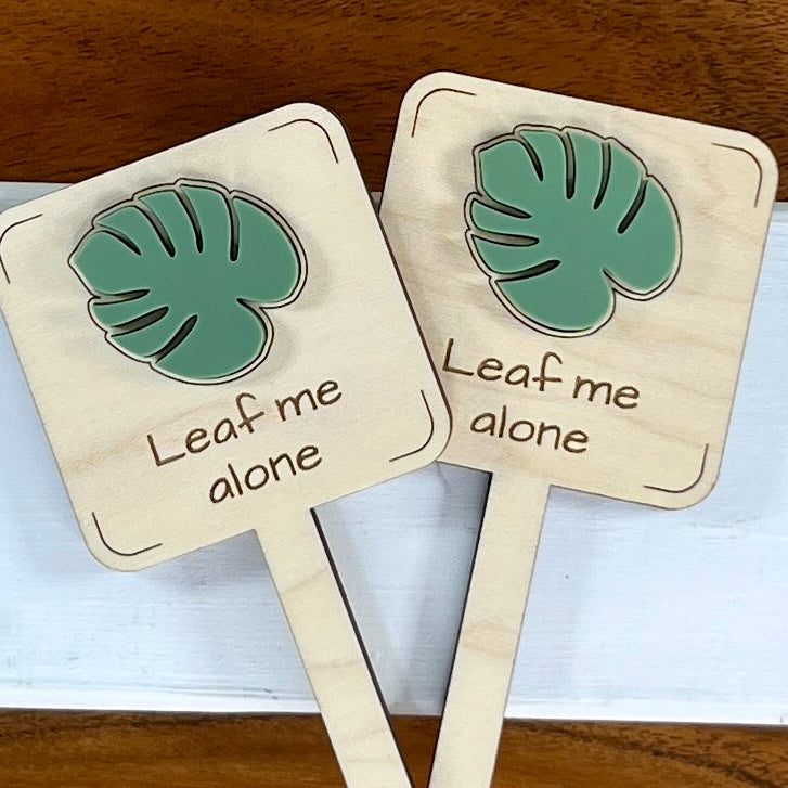 Two Leaf Me Alone maple wood plant stakes with sage green acrylic monstera leaf side by side