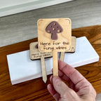Hand holding Here for the Fungi Vibes laser-cut maple wood plant stake with mauve acrylic mushroom