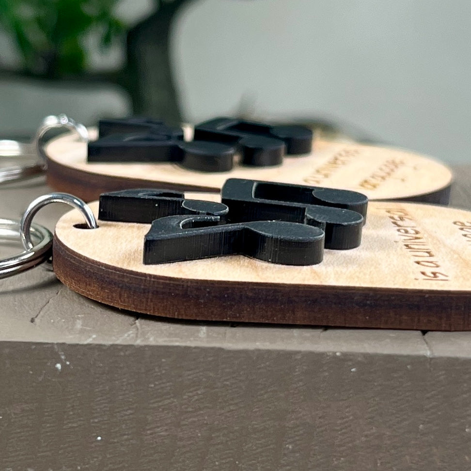 Side view close-up of laser-engraved wooden keychains with layered black acrylic musical notes, resting on a gray surface, showcasing the 3D effect.