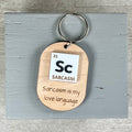 Sc Sarcasm Is My Love Language laser-engraved maple wood keychain with acrylic periodic table element detail on grey backdrop