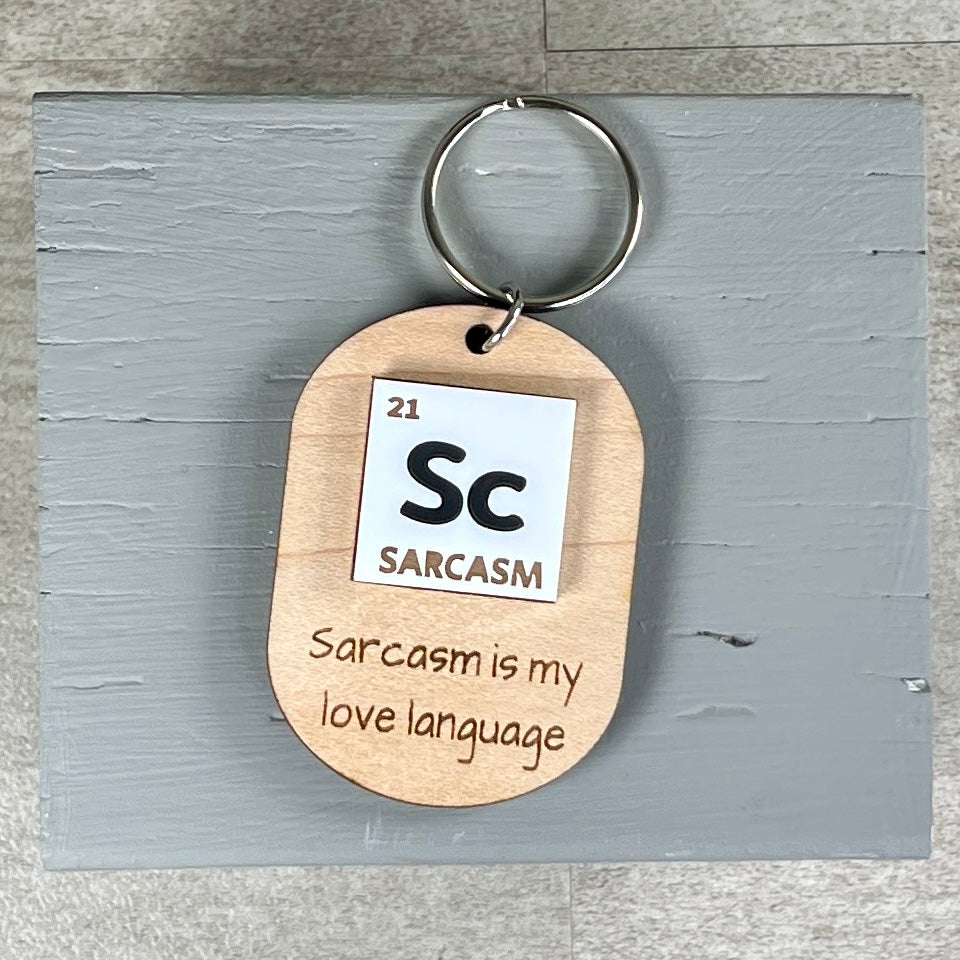 Sc Sarcasm Is My Love Language laser-engraved maple wood keychain with acrylic periodic table element detail on grey backdrop