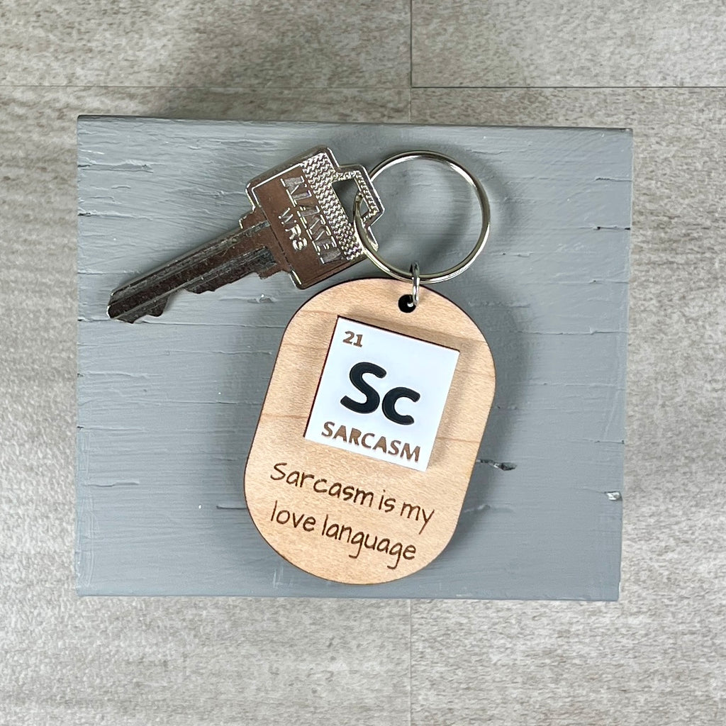 Sarcasm periodic table laser-engraved maple keychain with silver key ring on grey surface