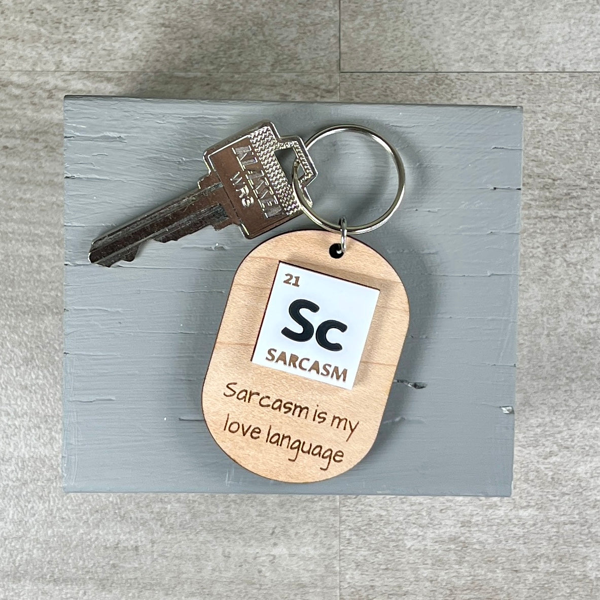 Sarcasm periodic table laser-engraved maple keychain with silver key ring on grey surface