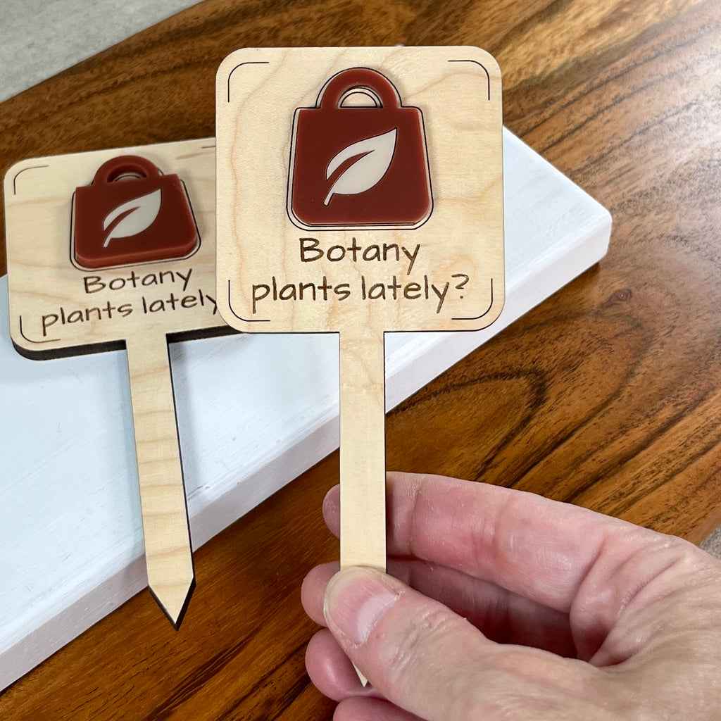 Hand holding Botany Plants Lately maple plant stakes showing rusty red and cool sand acrylic detail